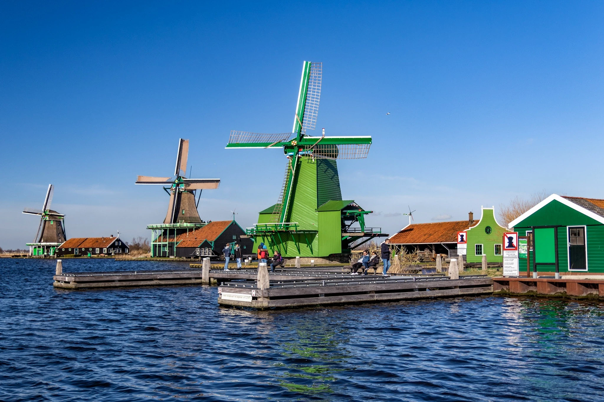 Traditional Dutch windmills and green wooden buildings beside a canal.