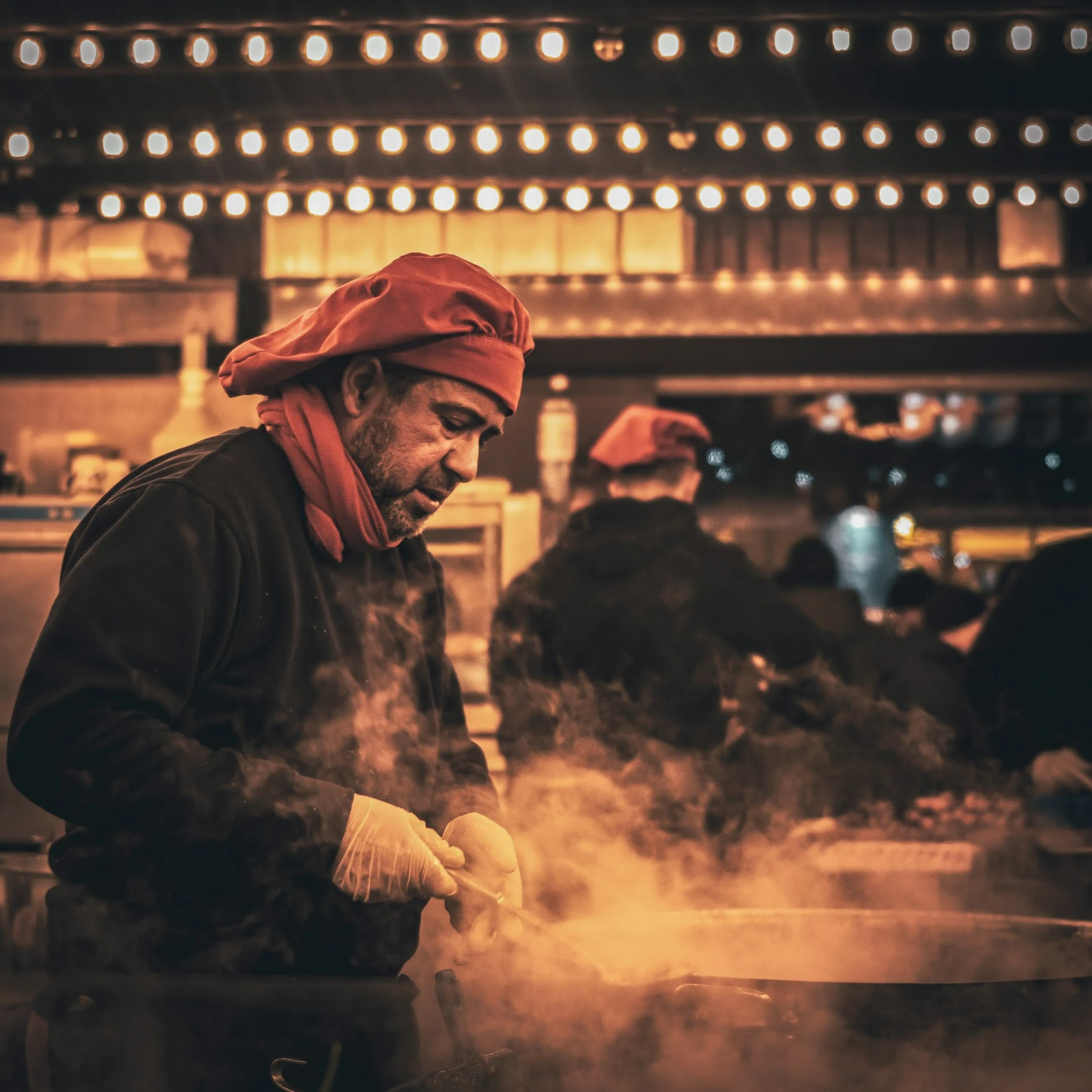 A market vendor working behind a cloud of steam under warm lights.