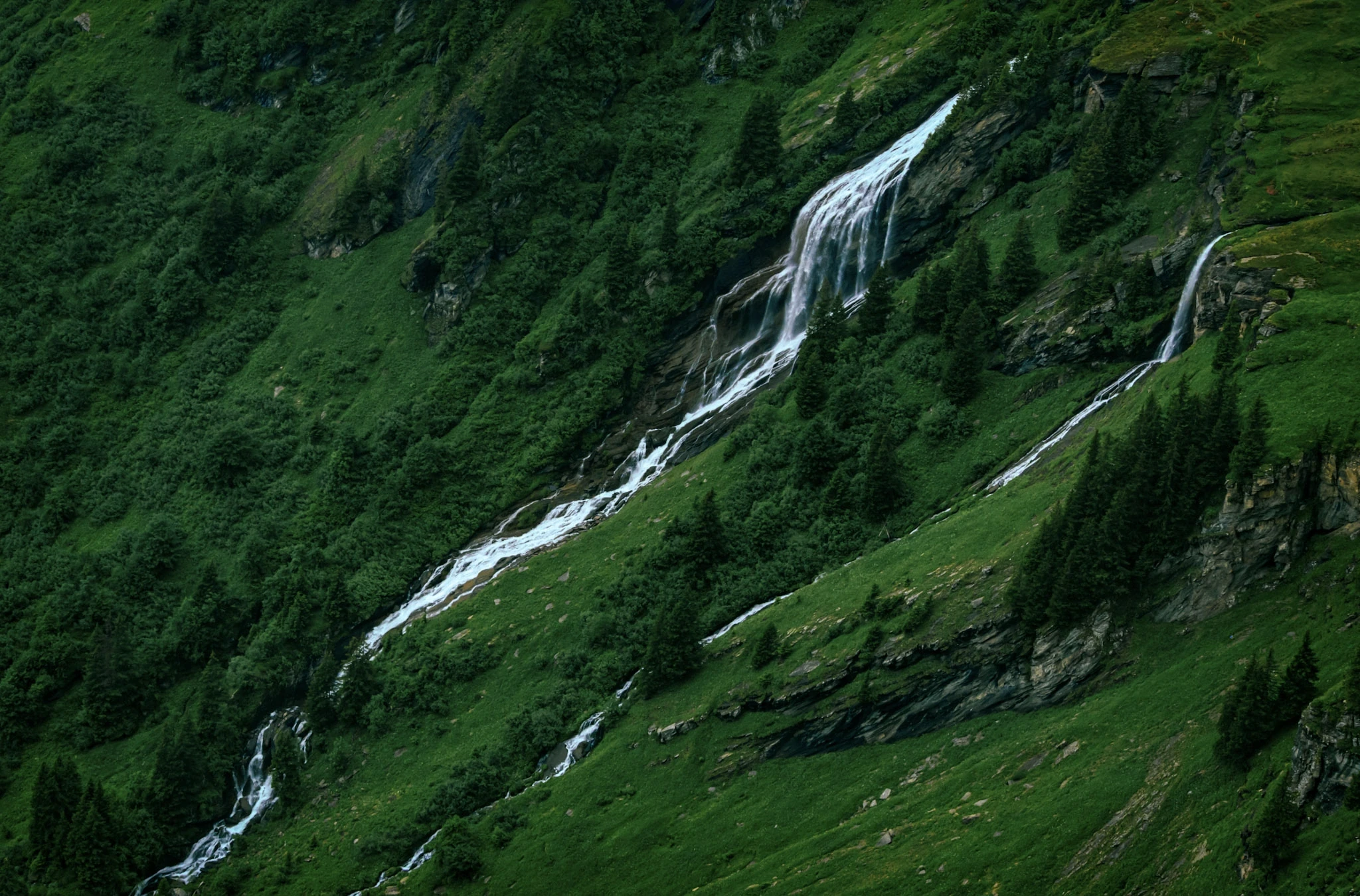 A narrow waterfall descending a steep, densely green mountainside.
