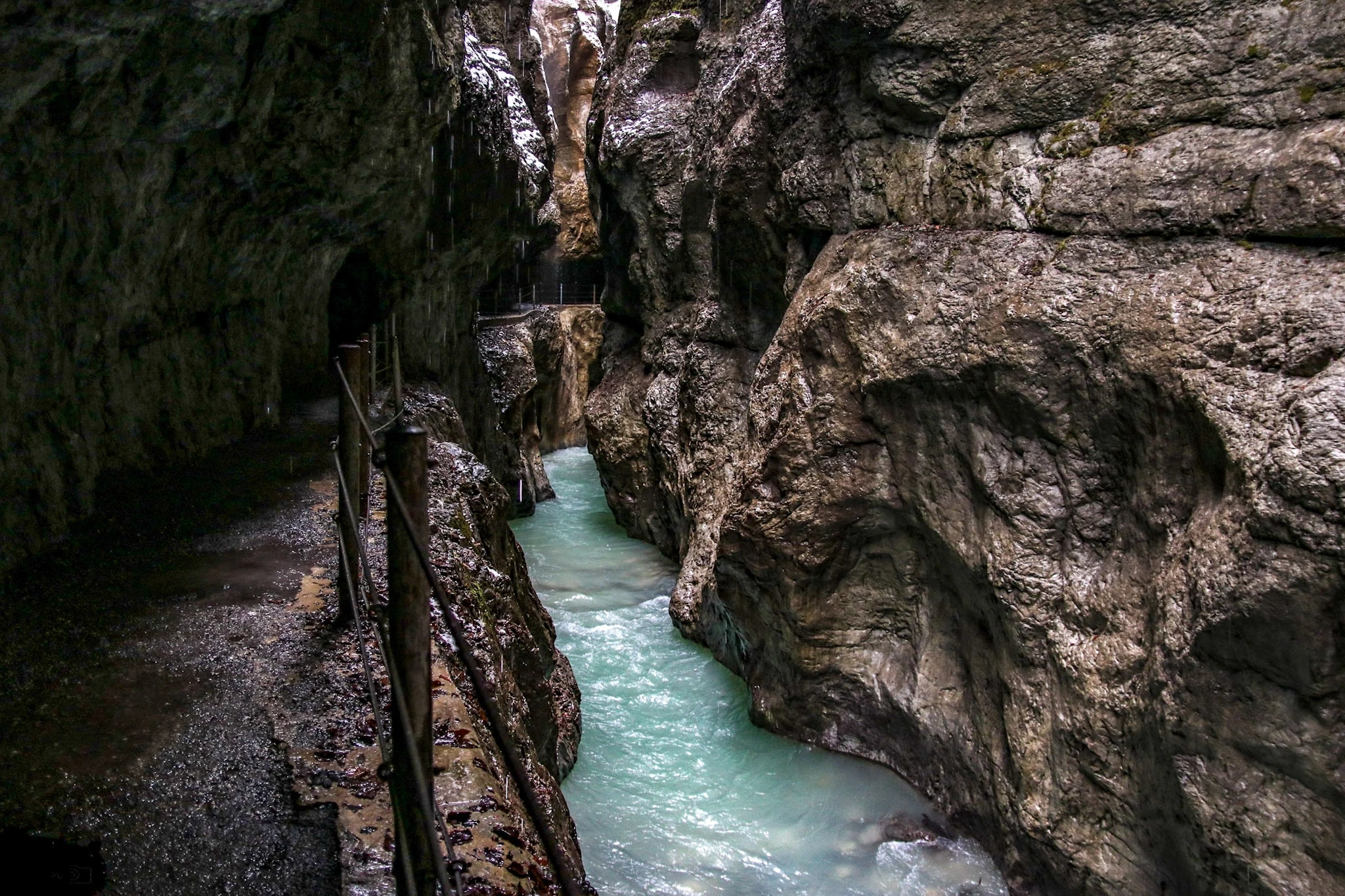 A narrow walkway following rushing water through a deep, rocky gorge.