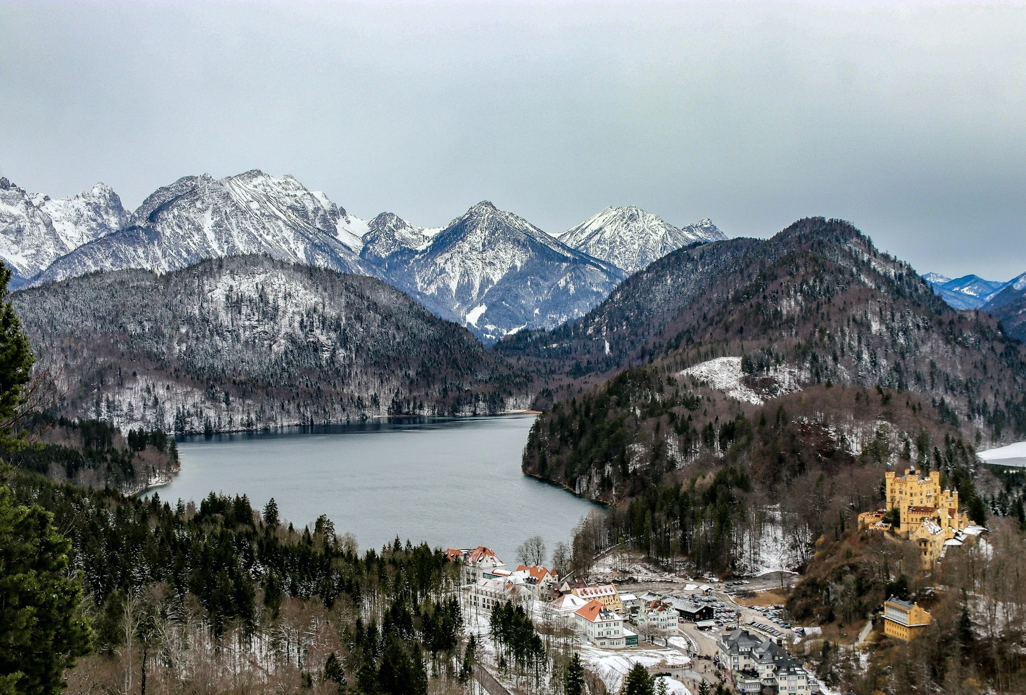A mountain lake and forest beneath rugged, snow-covered peaks.