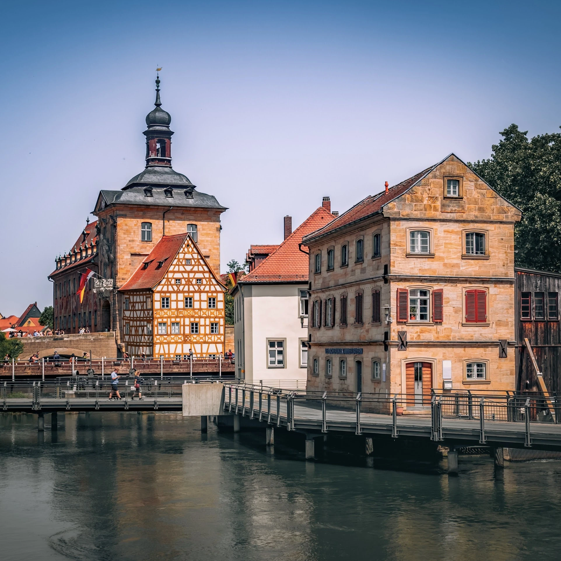 Historic buildings and a pointed tower reflected in still water.