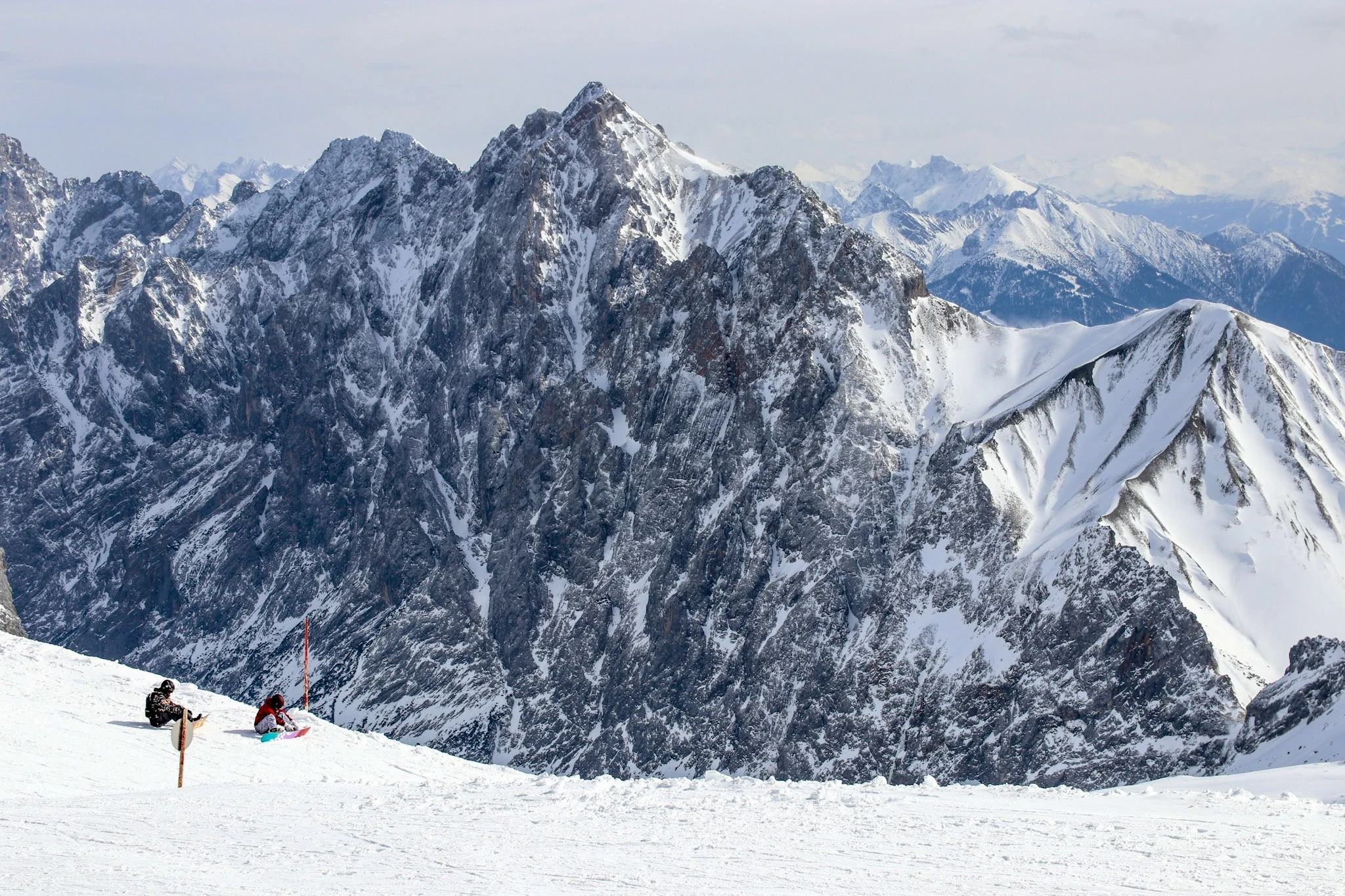 Skiers crossing a wide snowfield beneath a jagged Alpine ridge.