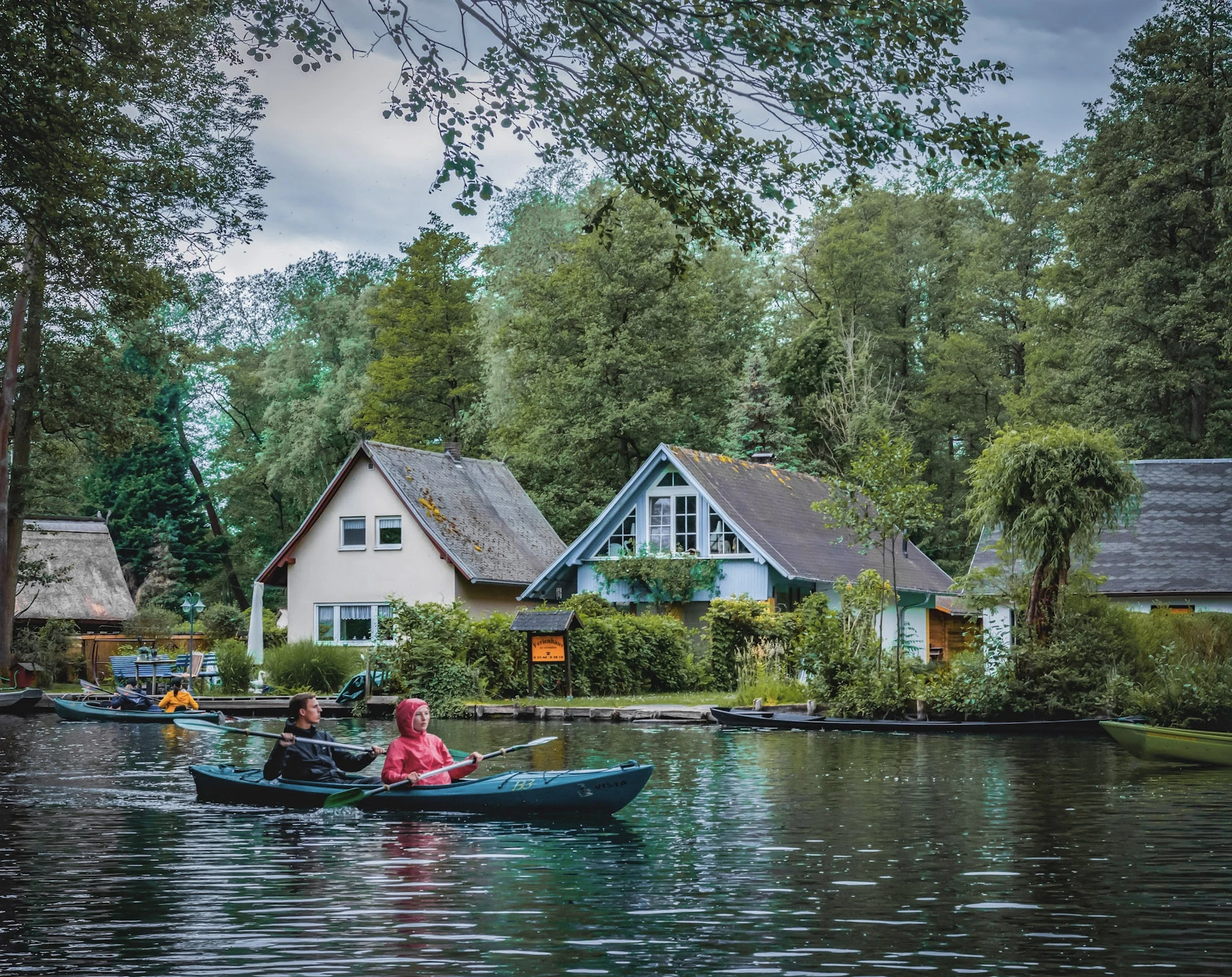 Two small wooden boathouses reflected in a calm lake surrounded by trees.