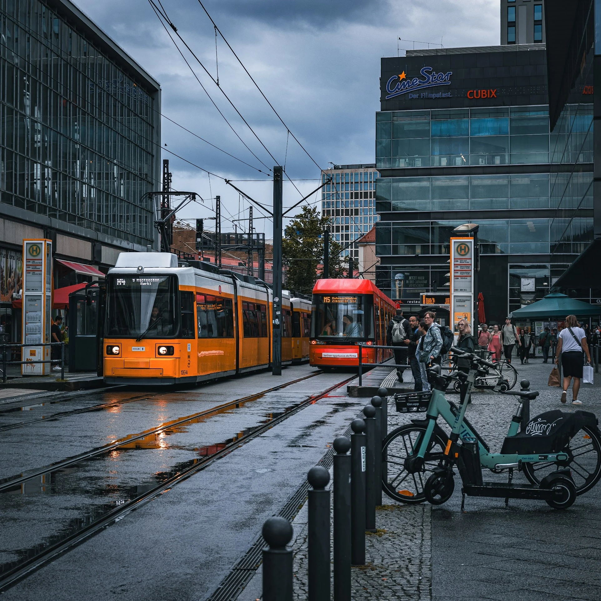 An orange tram passing modern city buildings beside parked bicycles.