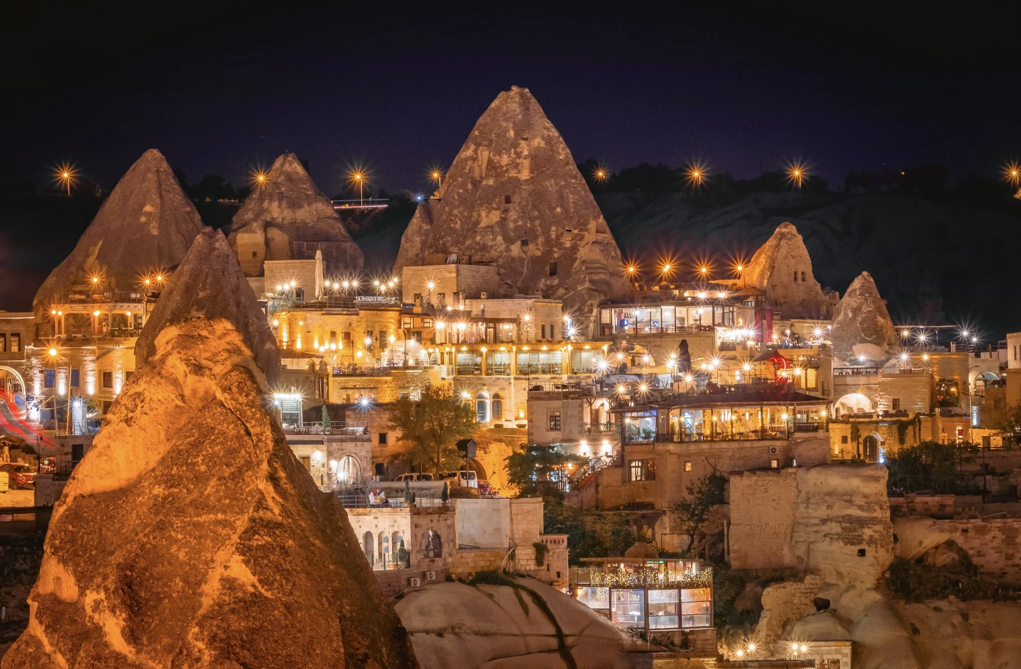 Illuminated buildings nestled among Cappadocia's distinctive rock formations at night.