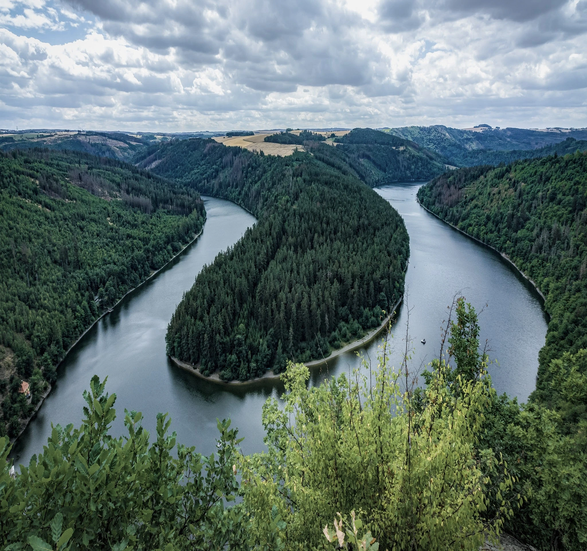 A broad river curving around a wooded peninsula beneath a cloudy sky.