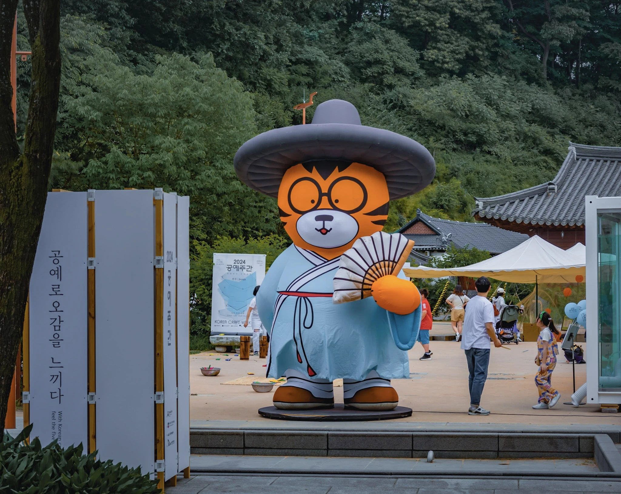 A cartoon tiger statue welcoming visitors beside traditional Korean buildings.