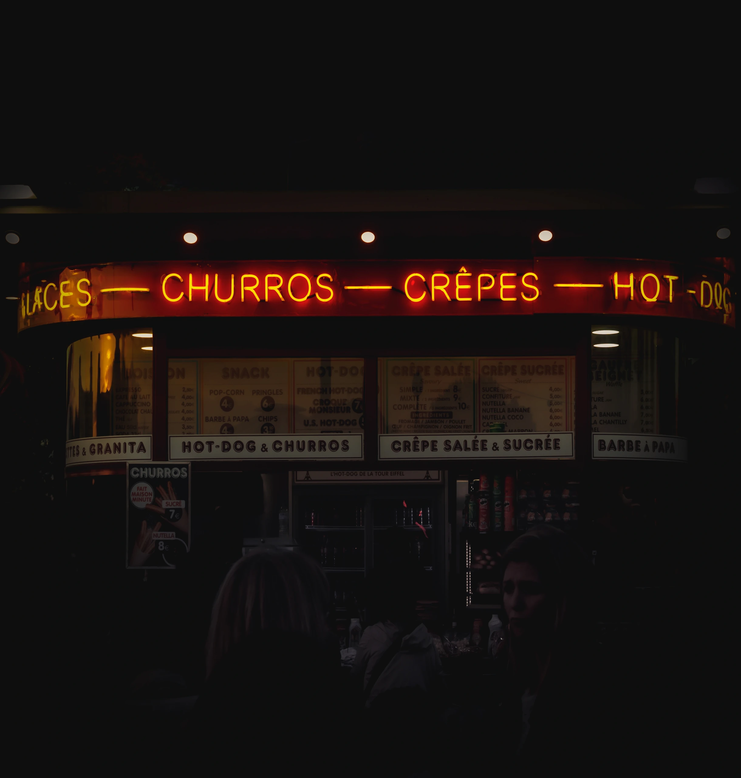A glowing churros and crêpes sign on a dark evening food stall.