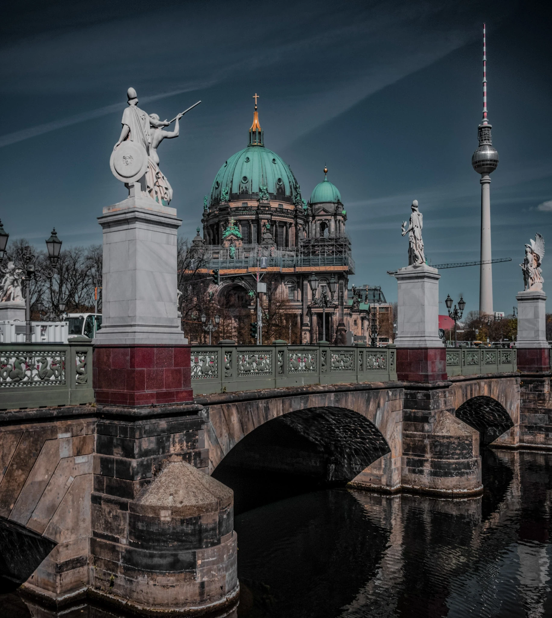 An ornate bridge sculpture with Berlin Cathedral and the television tower behind it.