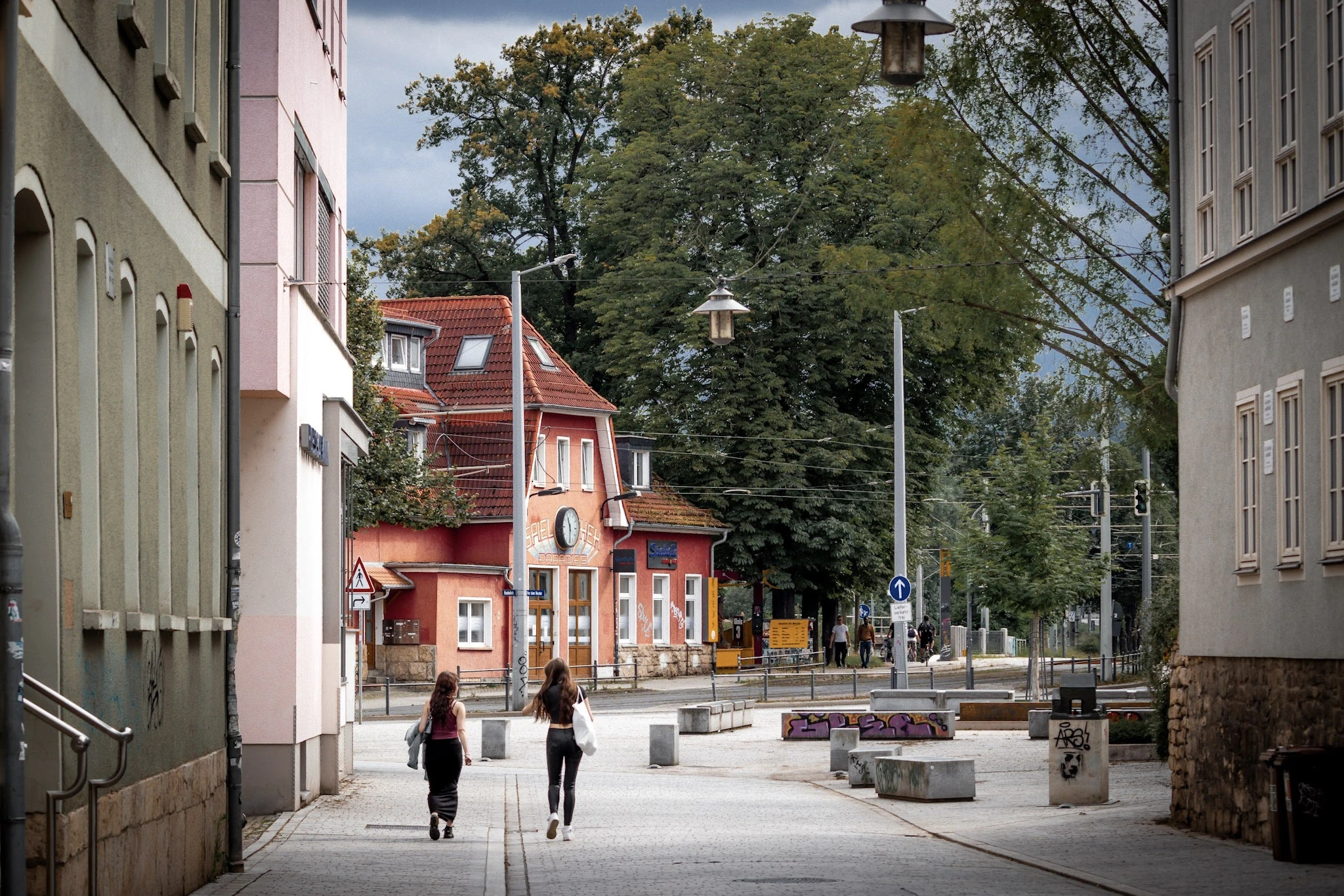 People walking between pastel buildings along a quiet pedestrian street.