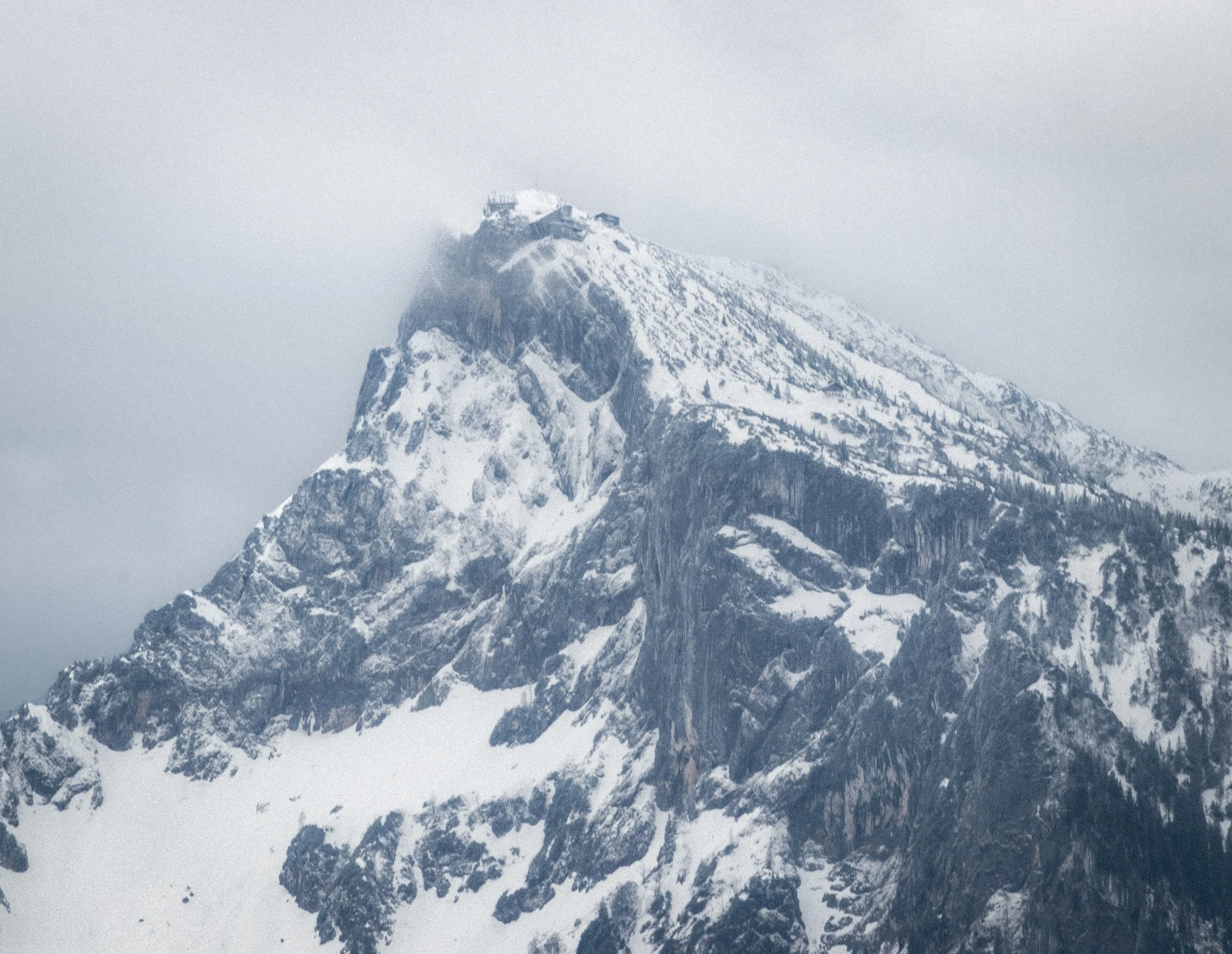 A snow-covered mountain peak partly hidden by low clouds.