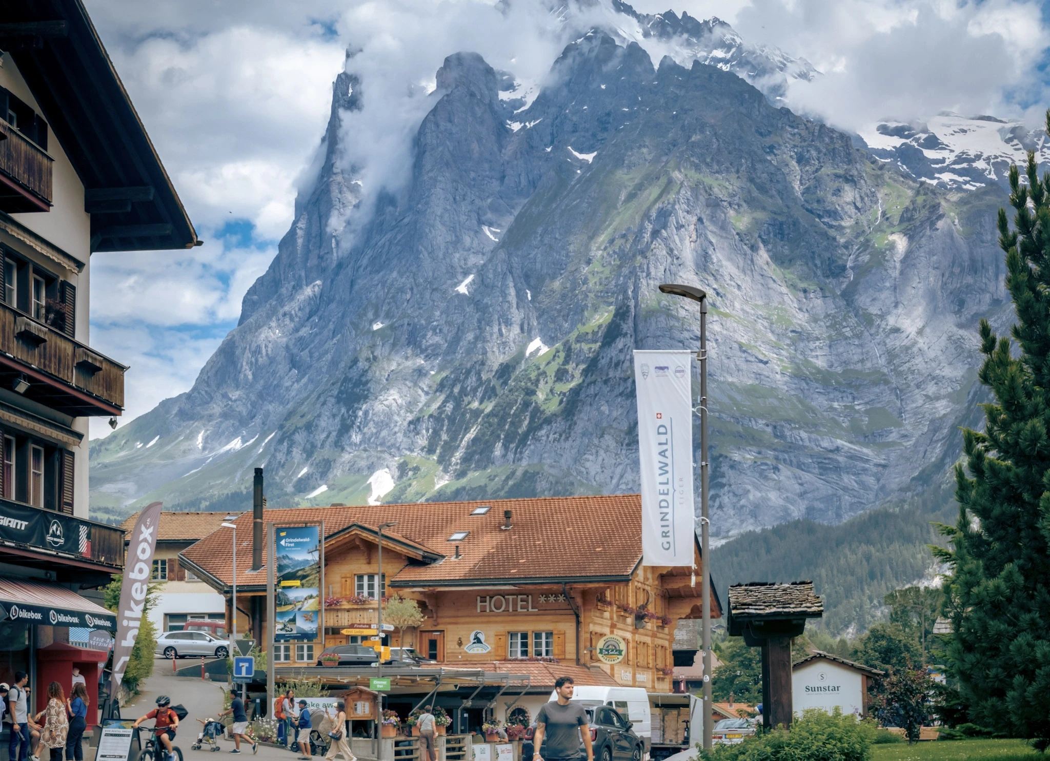 Wooden village buildings beneath sharply rising mountain peaks.