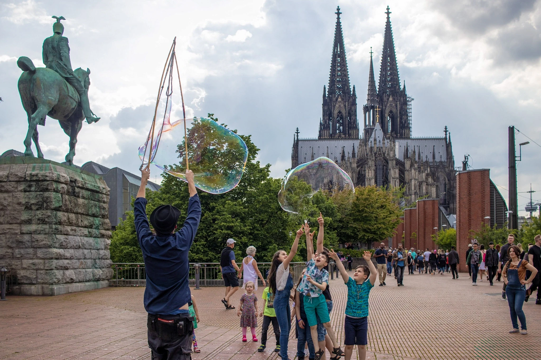 People playing with large soap bubbles beneath Cologne Cathedral's twin spires.