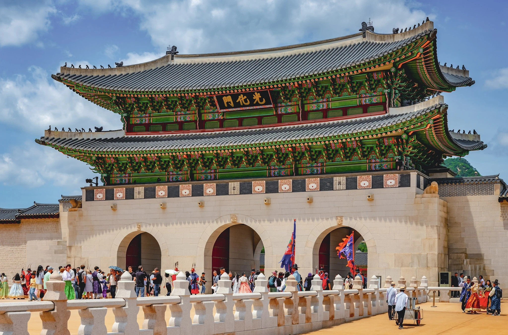 Visitors passing a large traditional Korean palace gate beneath a tiled roof.