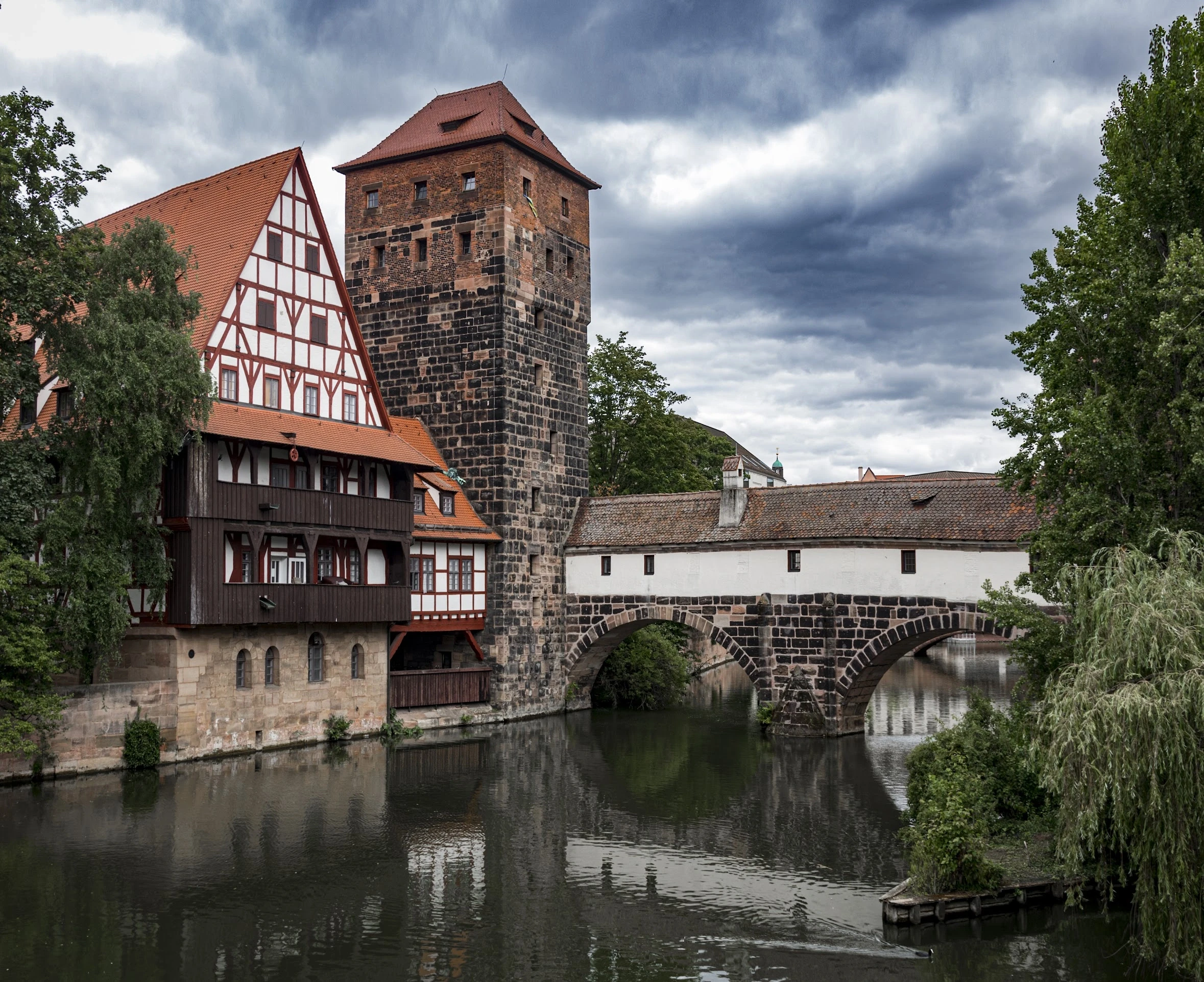 A timber-framed house reflected beside a stone bridge over a river.