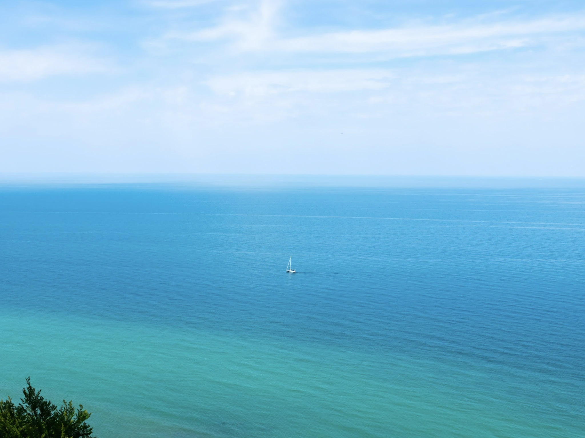 A small sailboat on a turquoise sea beneath a cloud-streaked sky.