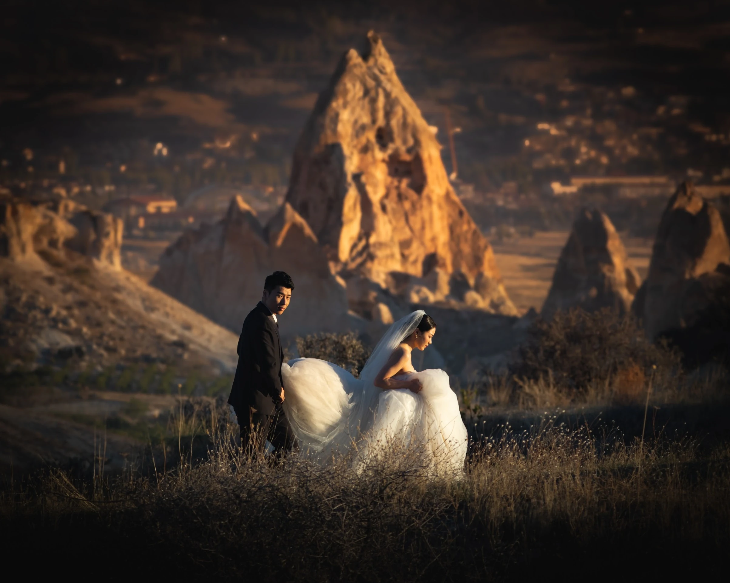 A couple posing beneath dramatic rock formations in warm evening light.