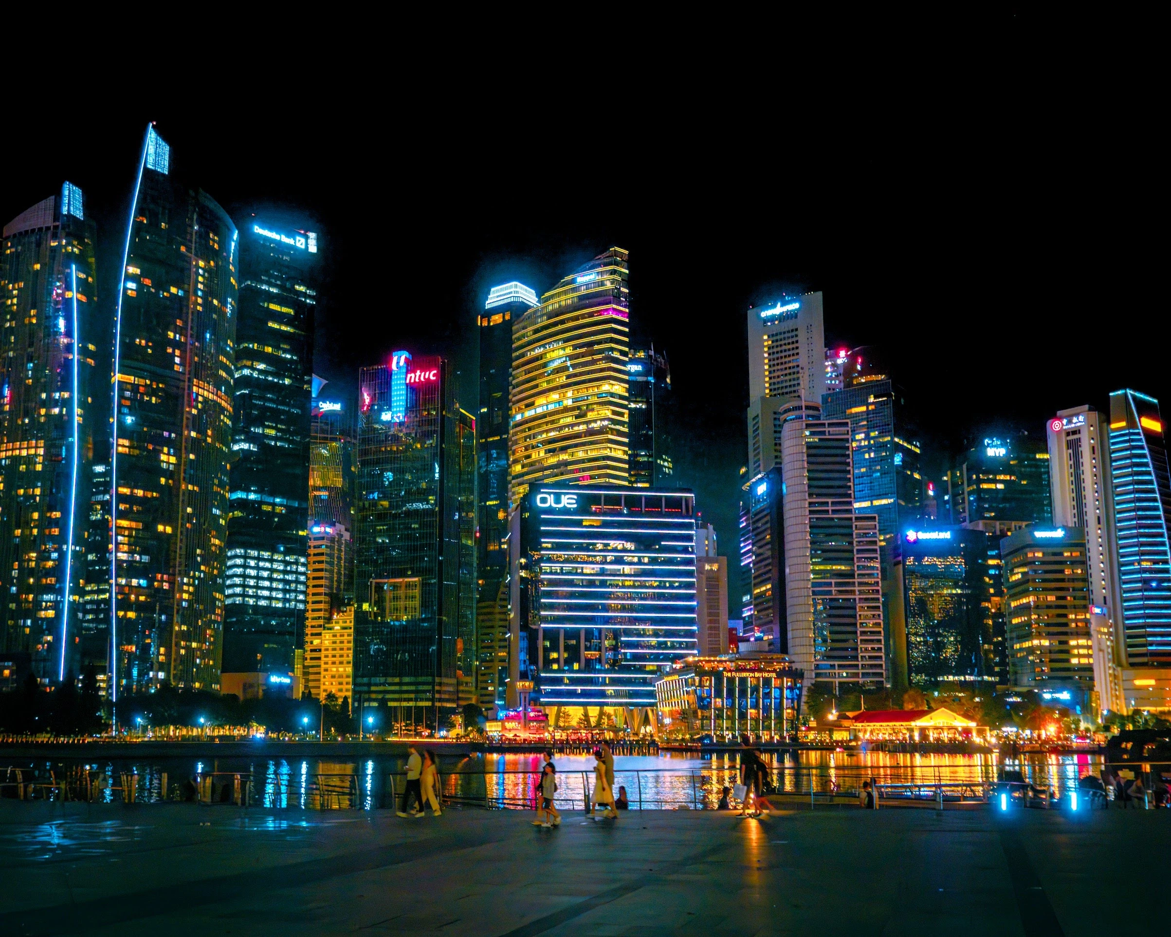 Illuminated Singapore waterfront towers reflected in dark water at night.