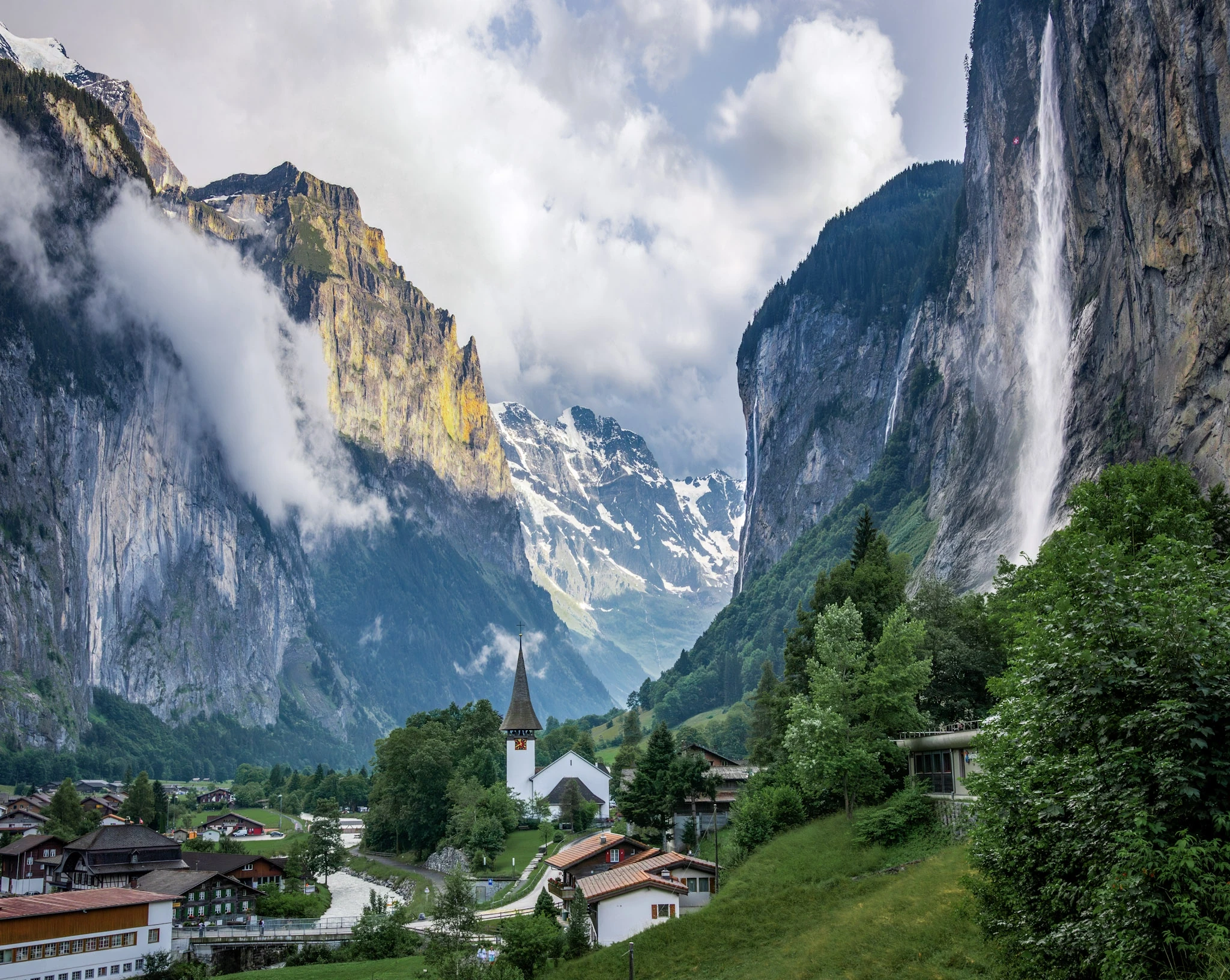 Village rooftops beneath a steep Alpine cliff and a high waterfall.