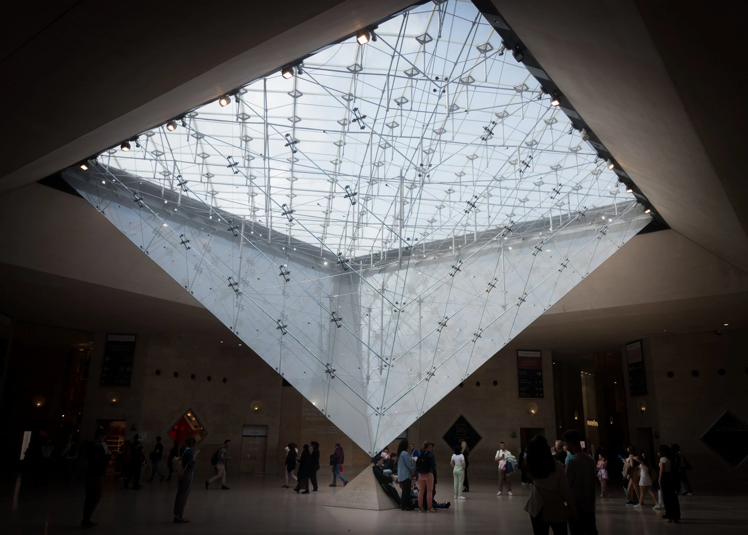 Visitors beneath the geometric glass structure of the Louvre pyramid.