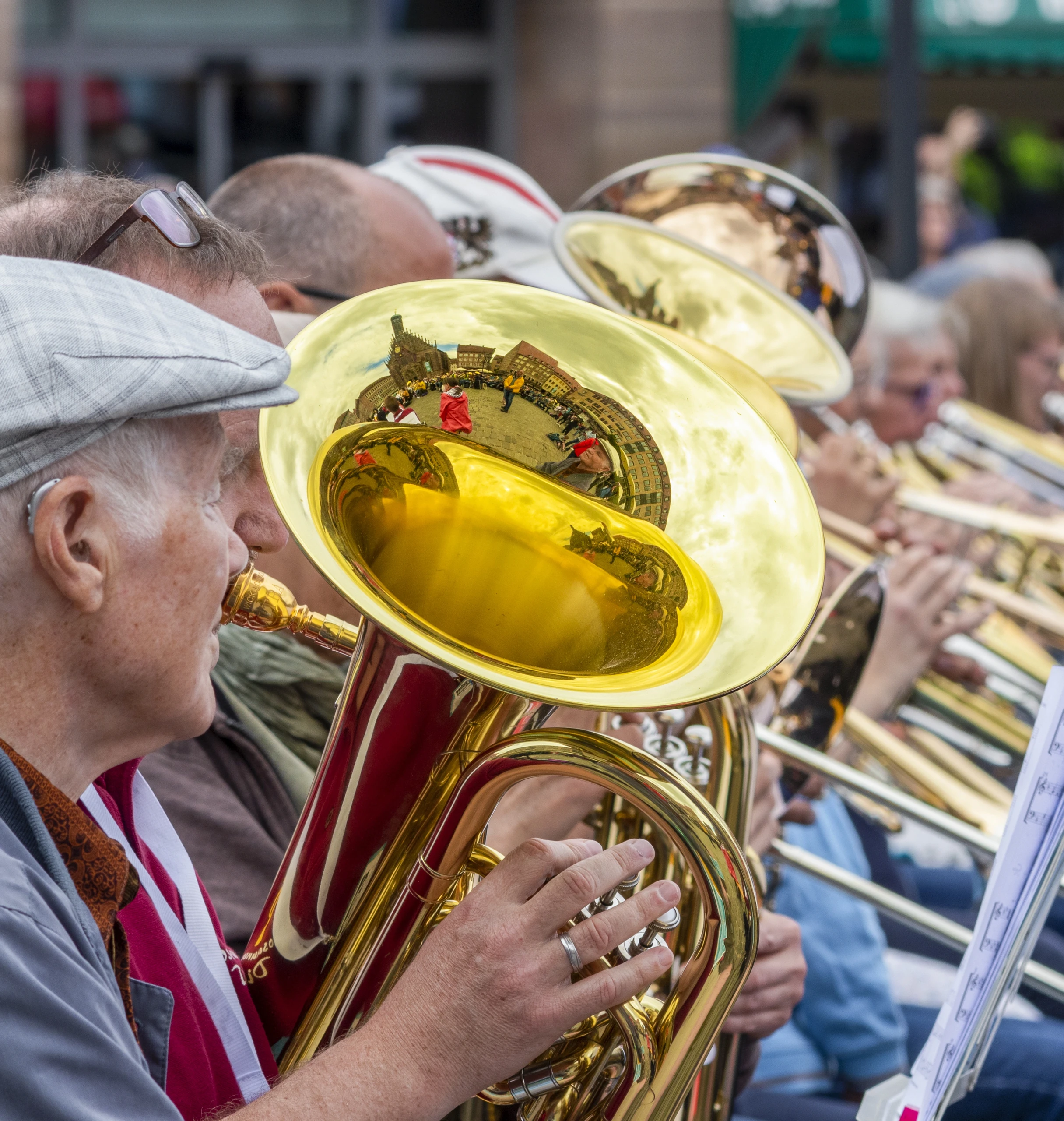 A musician playing a gleaming brass instrument among a crowd outdoors.